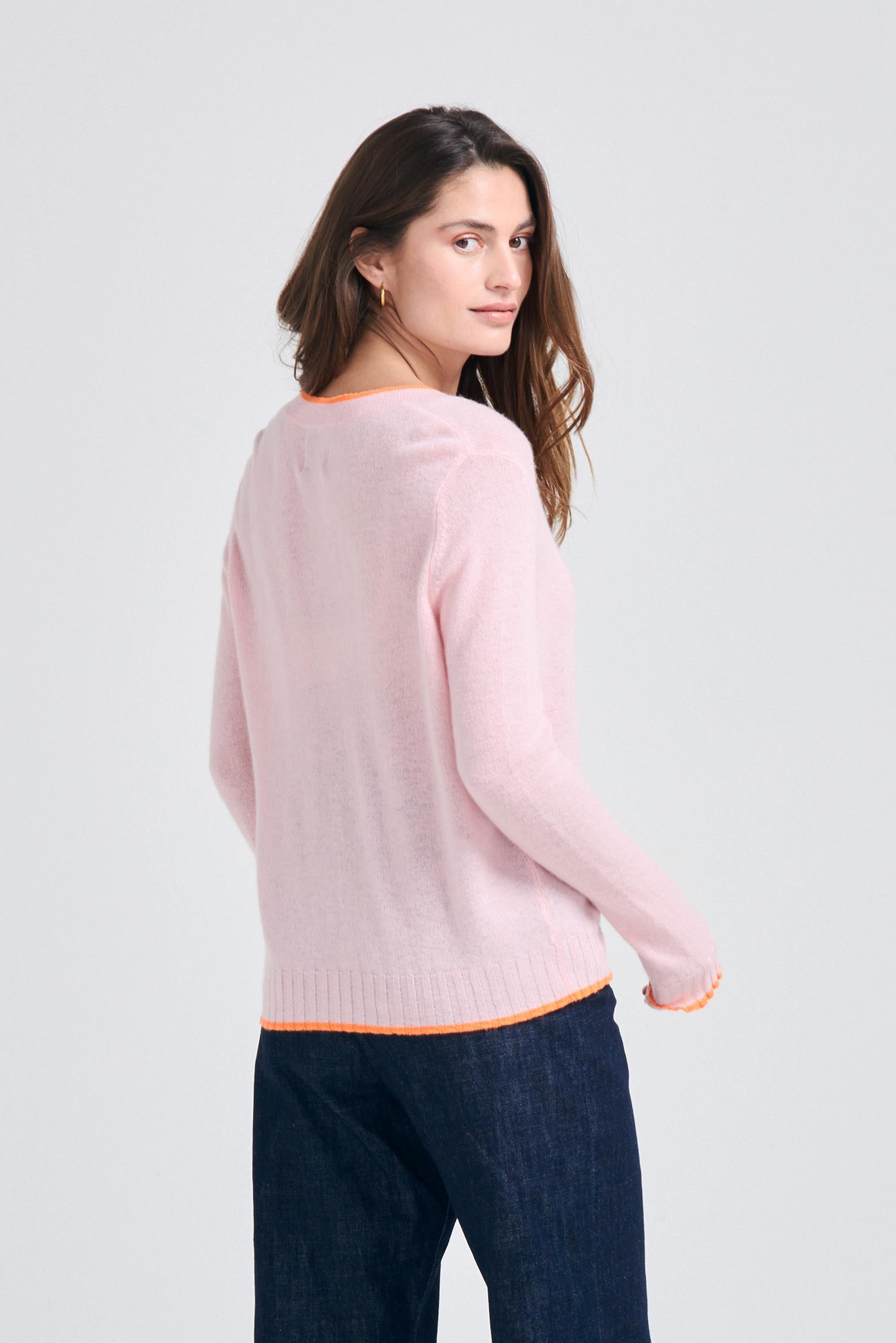Brown haired female model wearing Jumper1234 Pale pink cashmere vee neck cardigan with neon orange tipping facing away from the camera