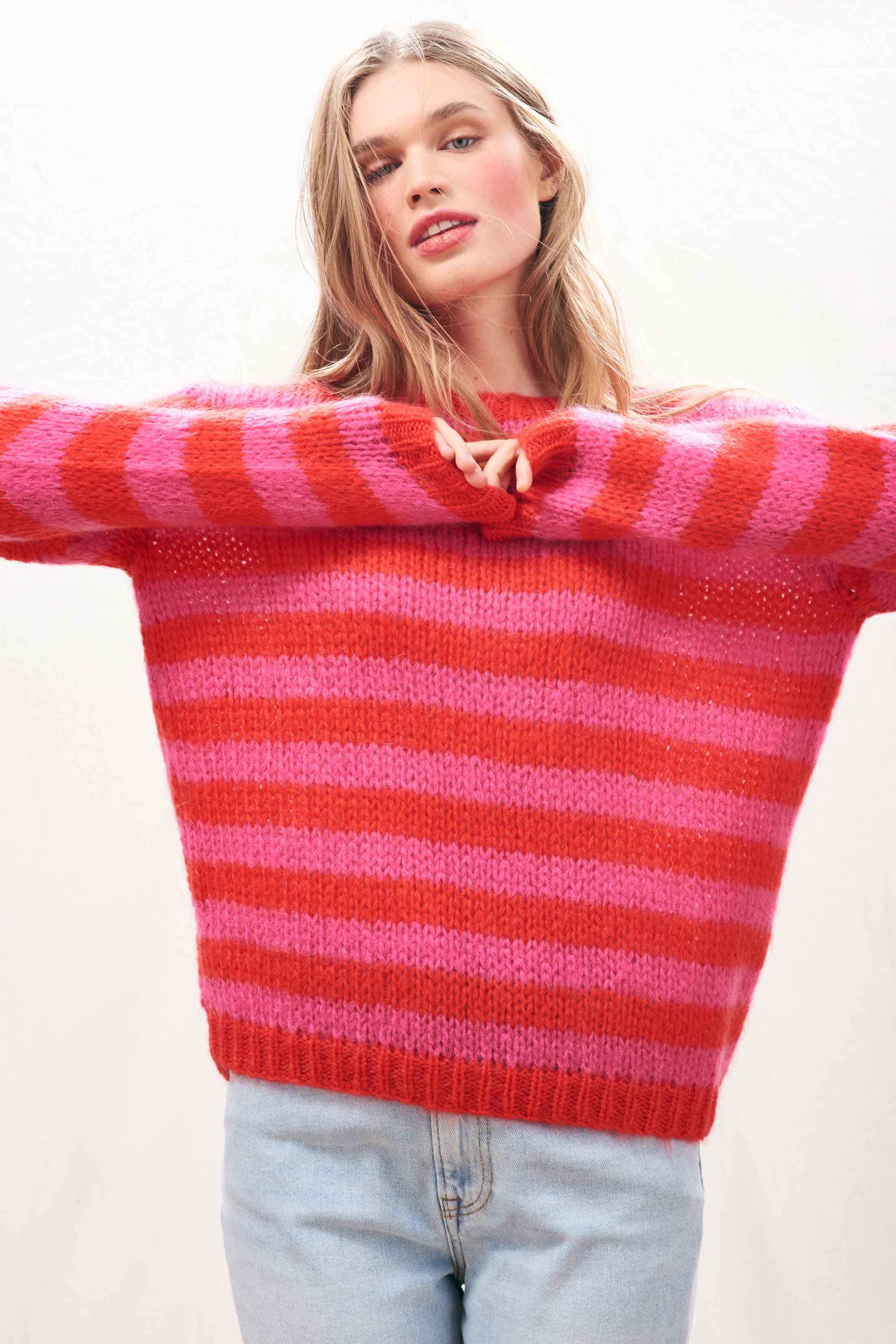 Female model wearing Jumper 1234 hand knitted mohair and wool blend hand knitted crew neck jumper in pink and red stripes.