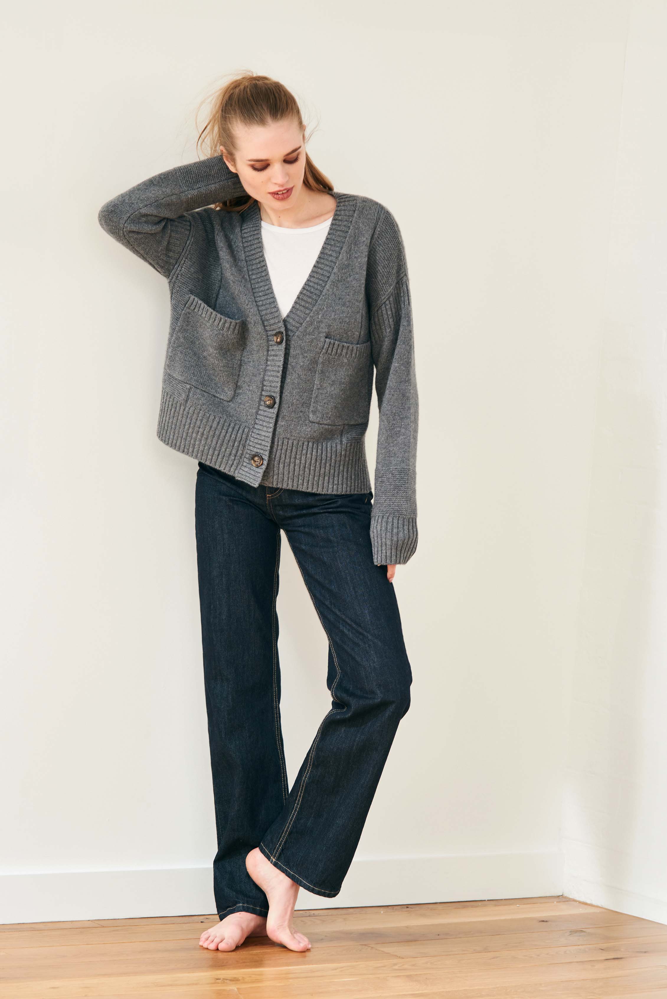 Female model wearing Jumper 1234 cashmere wool charcoal grey oversize vee neck cardigan with Guernsey details, splits at the sides and it's slightly longer at the back