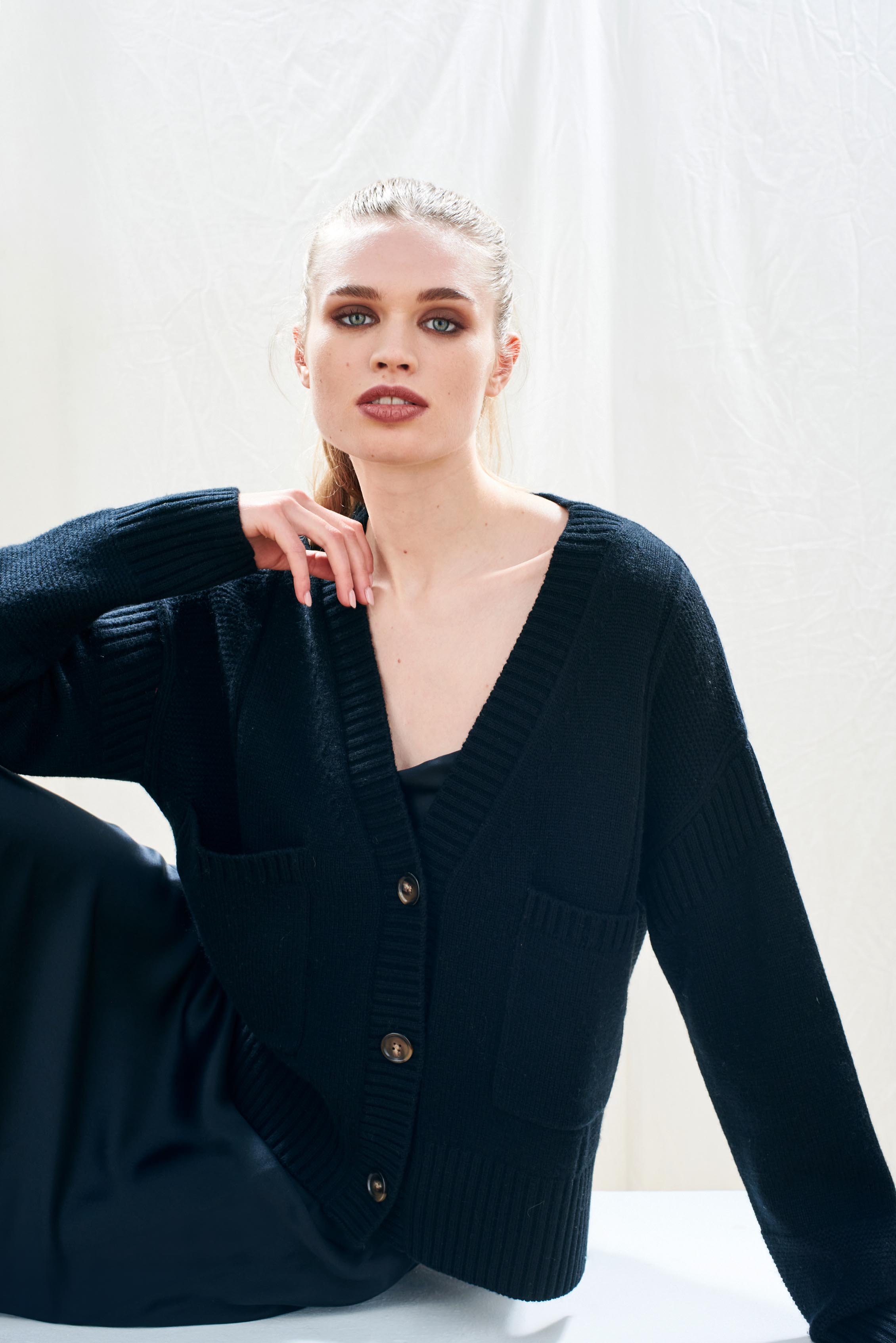 Female model wearing Jumper 1234 cashmere wool black oversize vee neck cardigan with Guernsey details, splits at the sides and it's slightly longer at the back