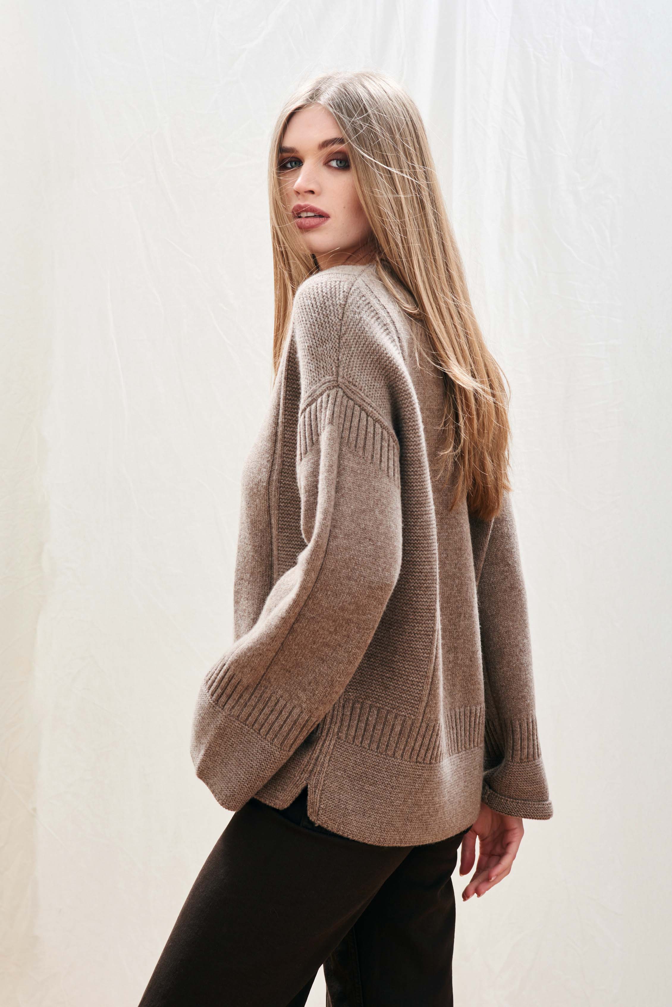 Female model wearing Jumper 1234 cashmere wool mid brown oversize jumper with guernsey details and trumpet sleeves facing away from the camera
