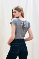 Female model wearing Jumper 1234 cap sleeve mid grey cashmere crew neck jumper with ribbon tie detail at the back facing away from the camera