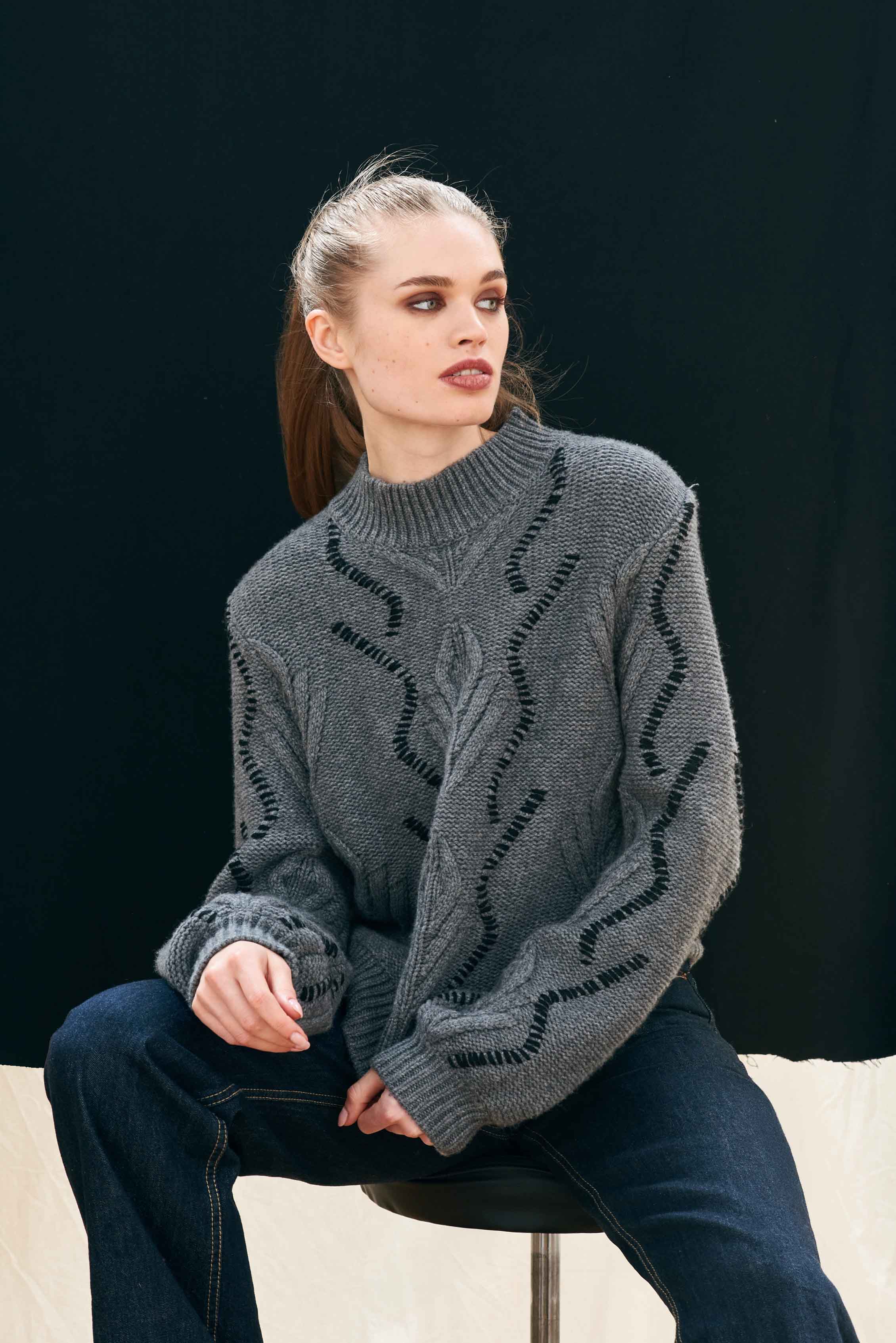 Female model wearing Jumper 1234 cashmere and wool jumper heavy weight Aran jumper in charcoal grey with black stitch detail, balloon sleeves and a turtle neck