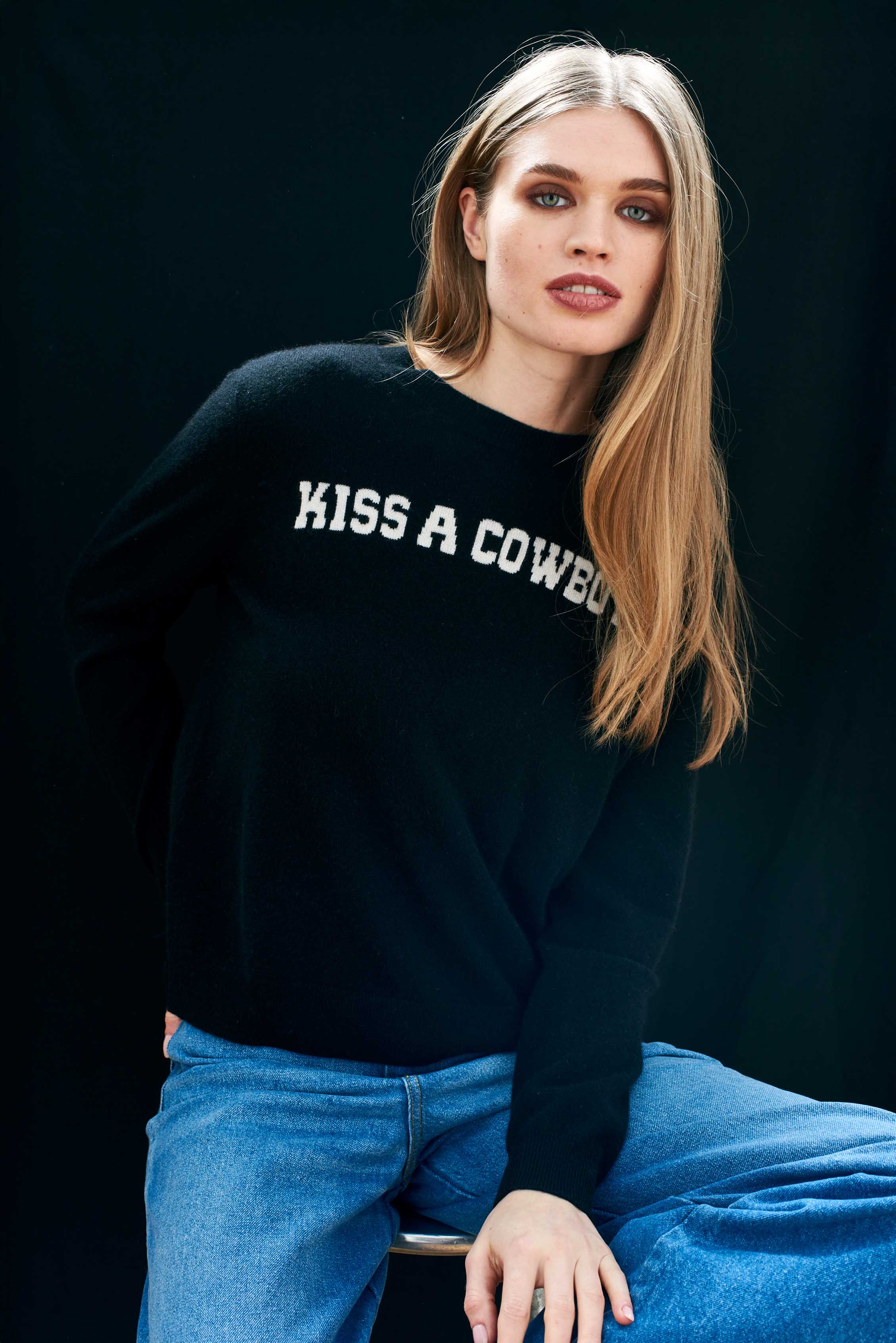 Female model wearing Jumper1234 cashmere black crew neck jumper with cream 'kiss a cowboy' intarsia
