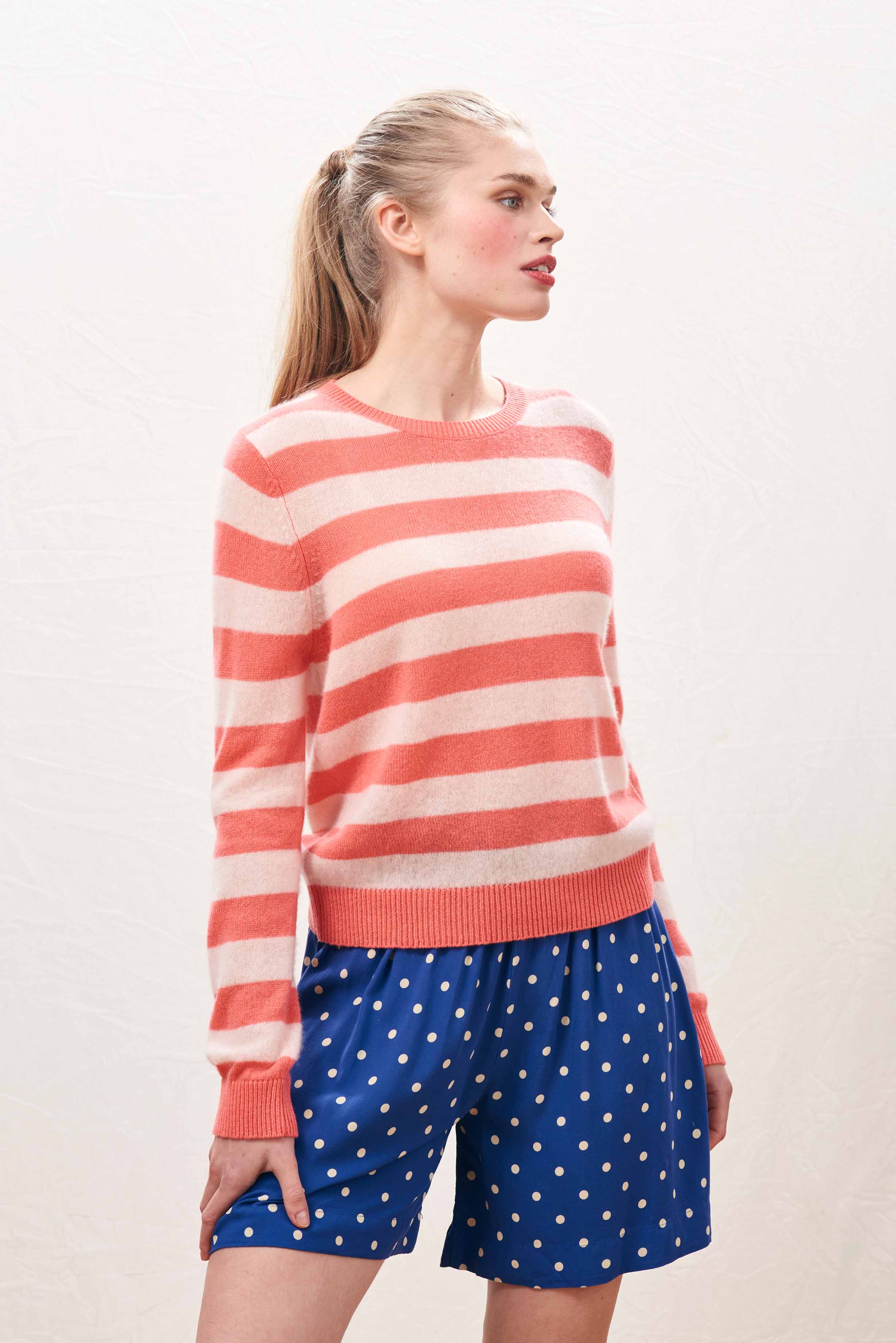 Female model wearing Jumper 1234 lightweight cashmere stripe crew neck in coral and pale pink.