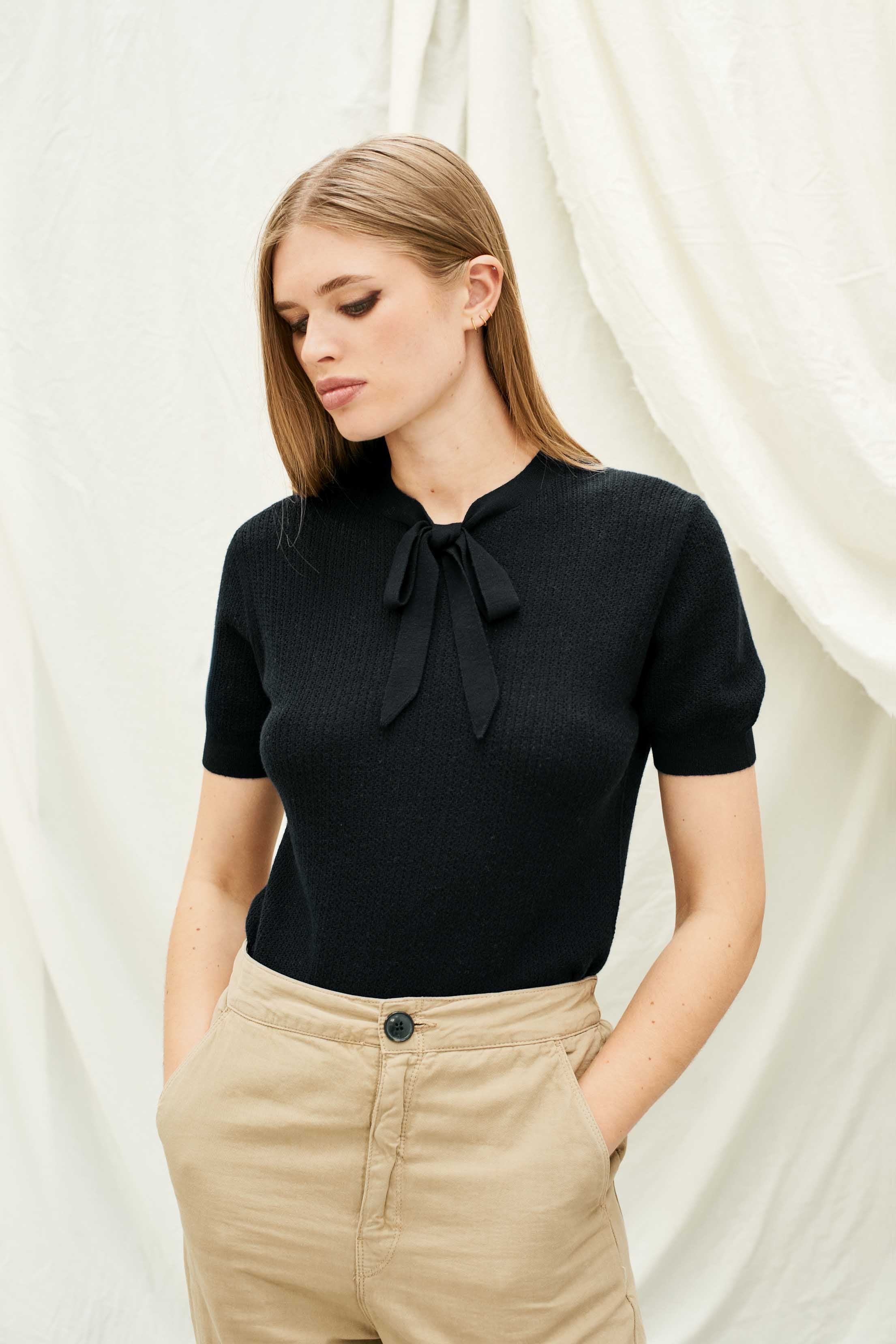 Female model wearing Jumper 1234 Black pointelle merino short sleeve jumper with a tie bow.