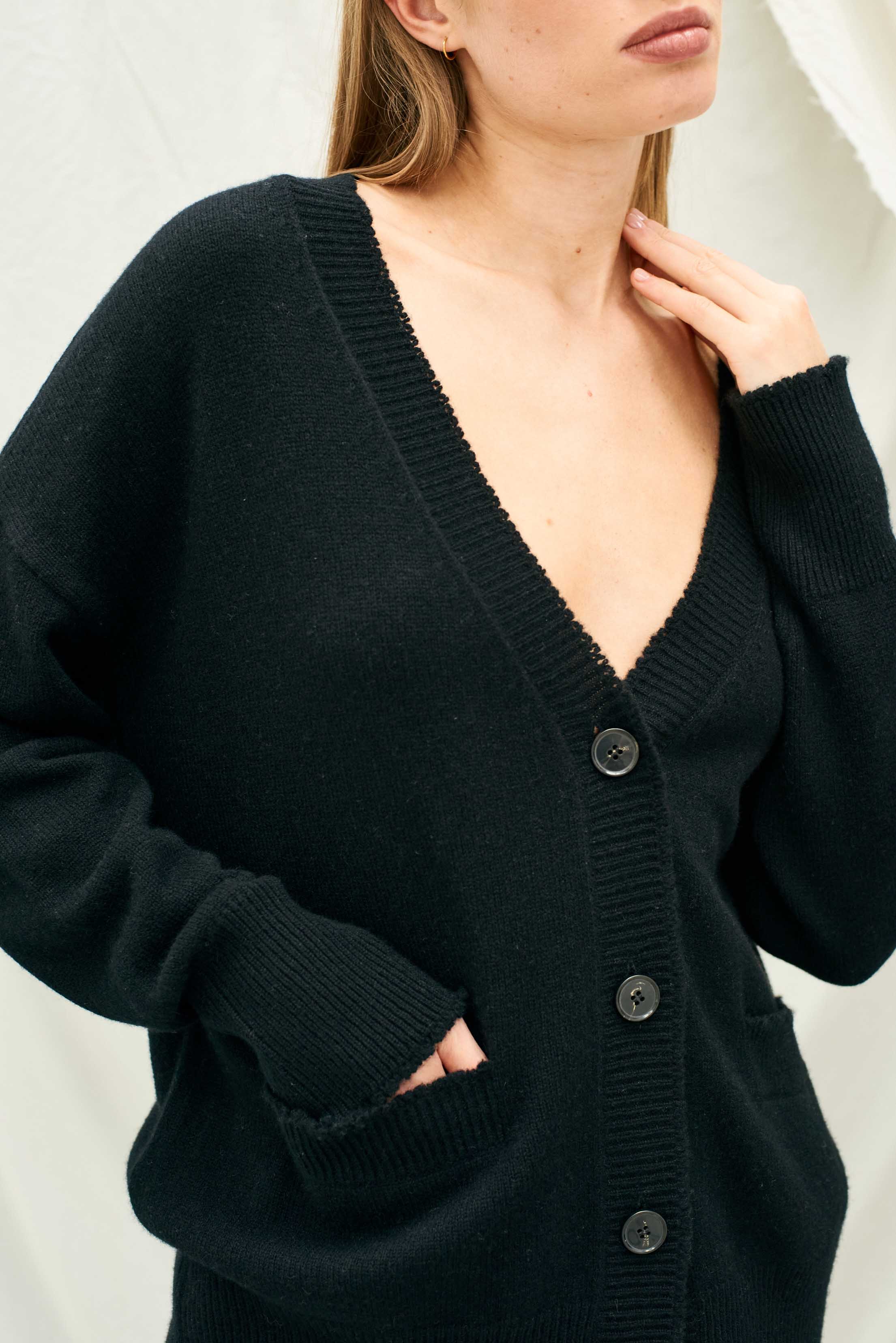 Female model wearing Jumper 1234 Heavier weight vee neck cardigan in black. Oversize fit with distressed ribs.