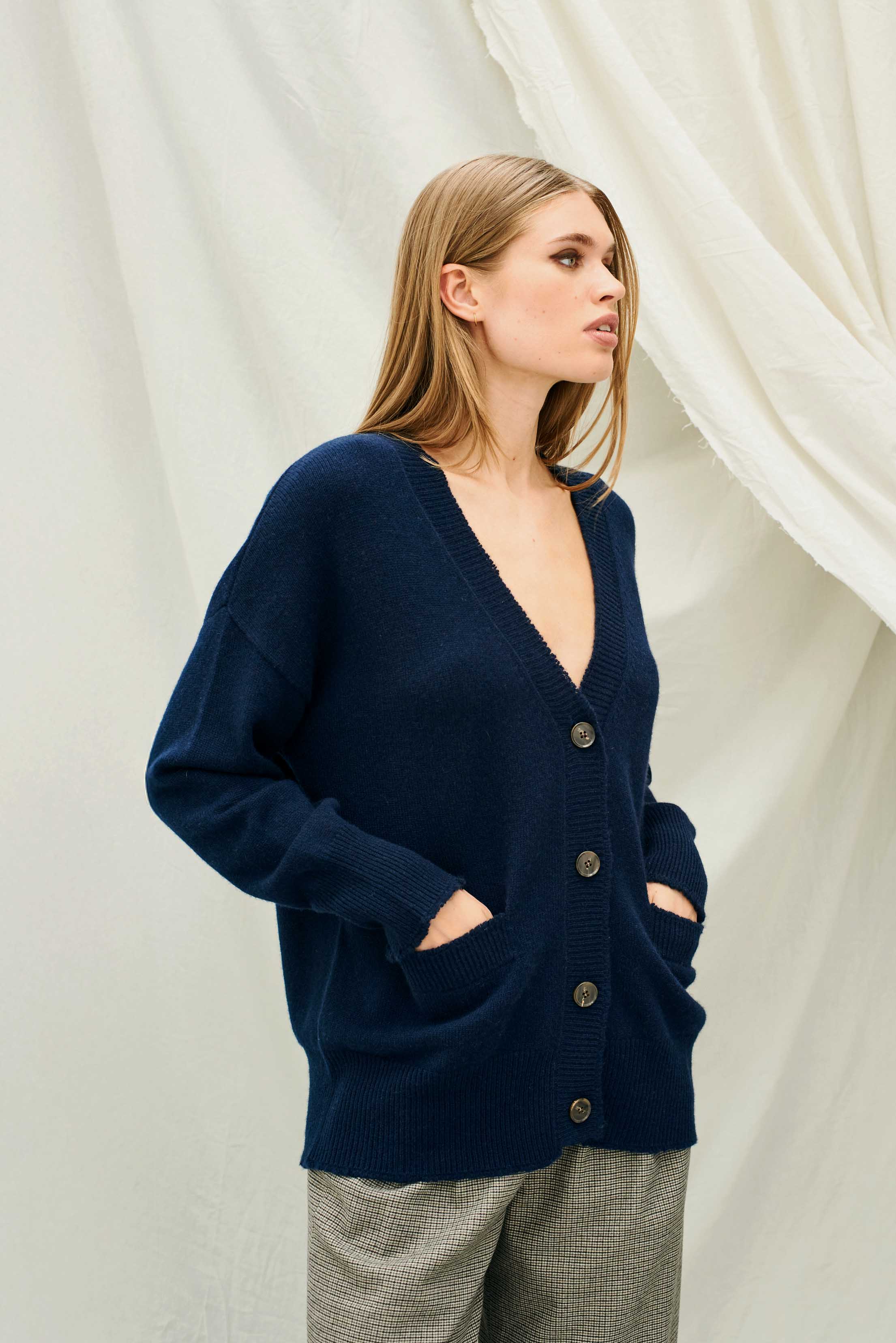 Female model wearing Jumper 1234 Heavier weight vee neck cardigan in navy. Oversize fit with distressed ribs.
