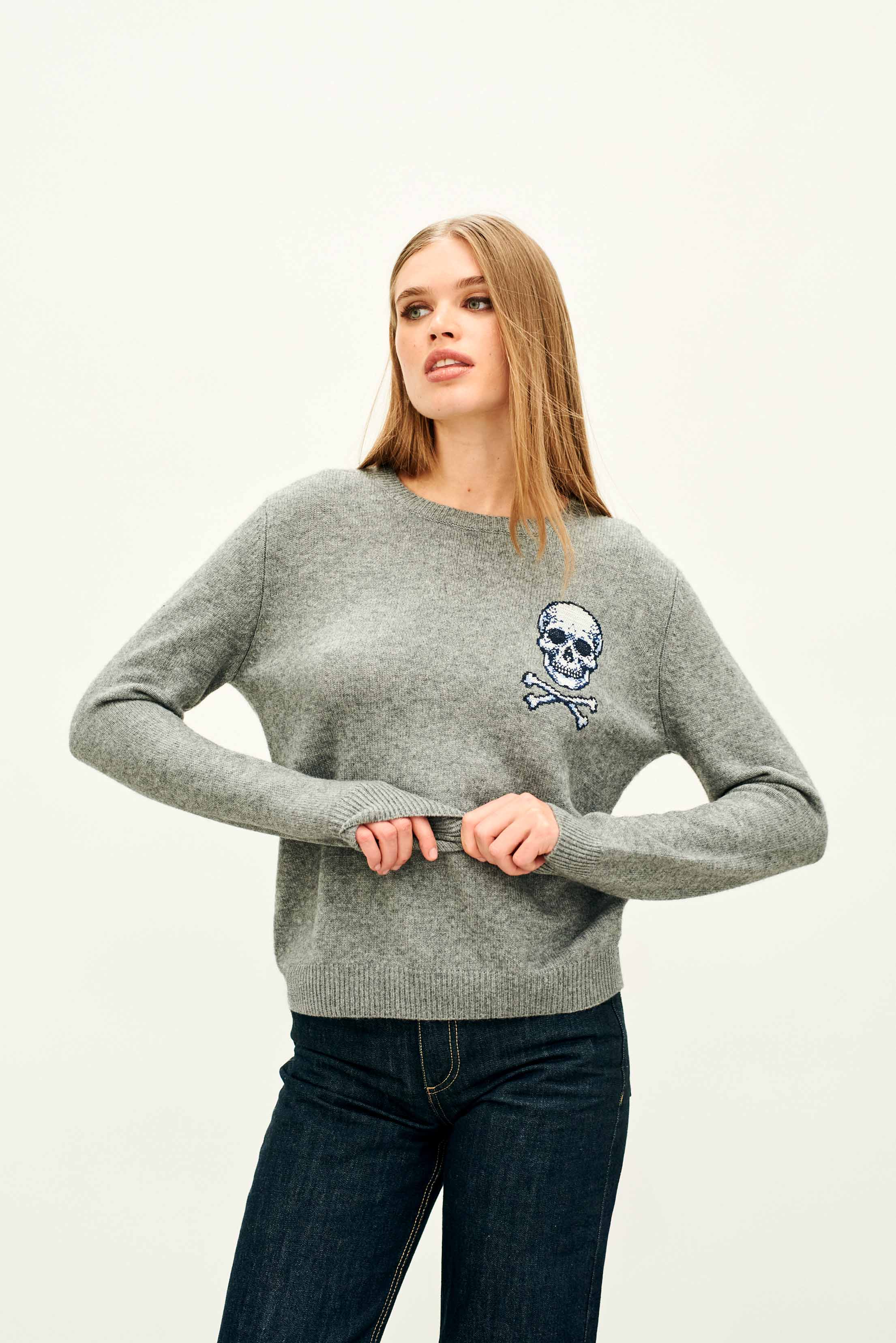 Female model wearing Jumper 1234 Mid grey crew neck jumper in cashmere and wool, with an embroidered skull and crossbones on the chest.
