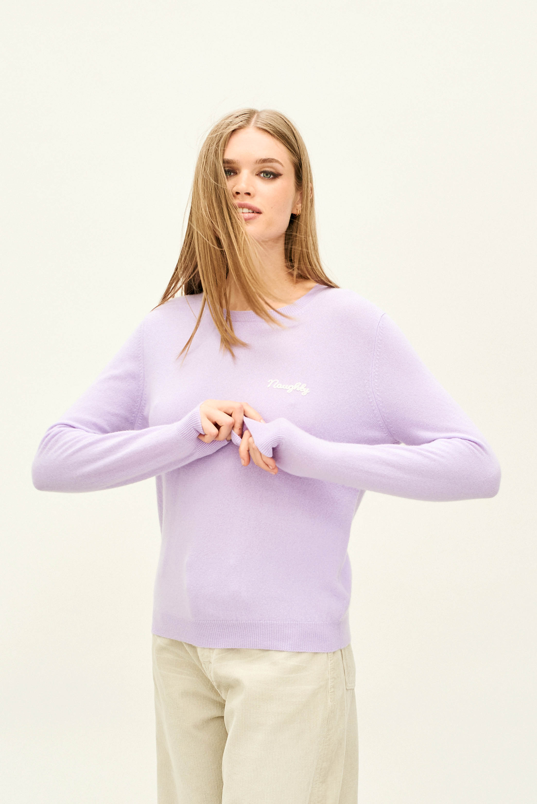 Female model wearing Jumper 1234 Lilac cashmere crew neck jumper with cream 'naughty' chain stitch embroidery on the chest and 'but nice' on the back.
