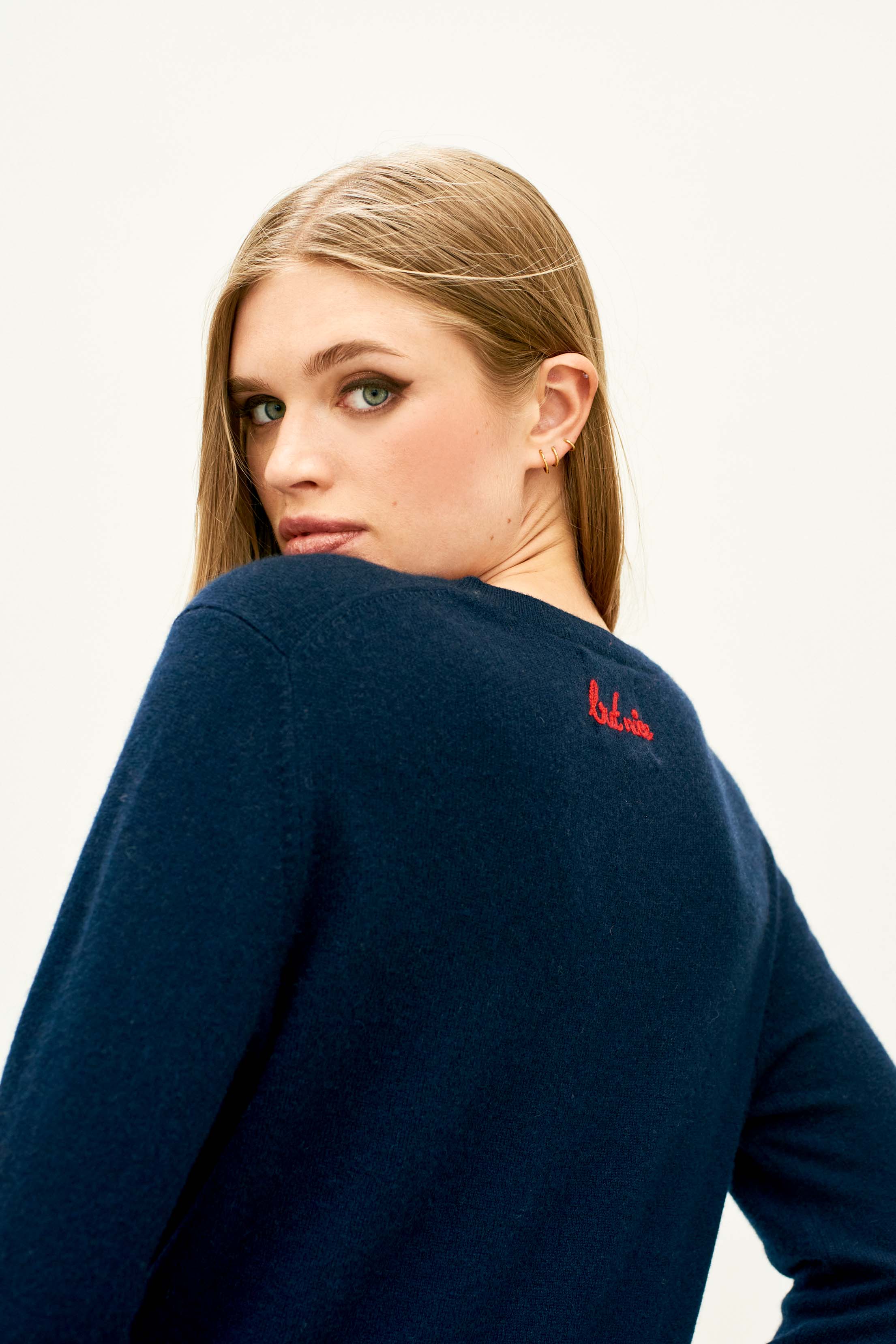 Female model wearing Jumper 1234 Navy cashmere crew neck jumper with red 'naughty' chain stitch embroidery on the chest and 'but nice' on the back. Back shot