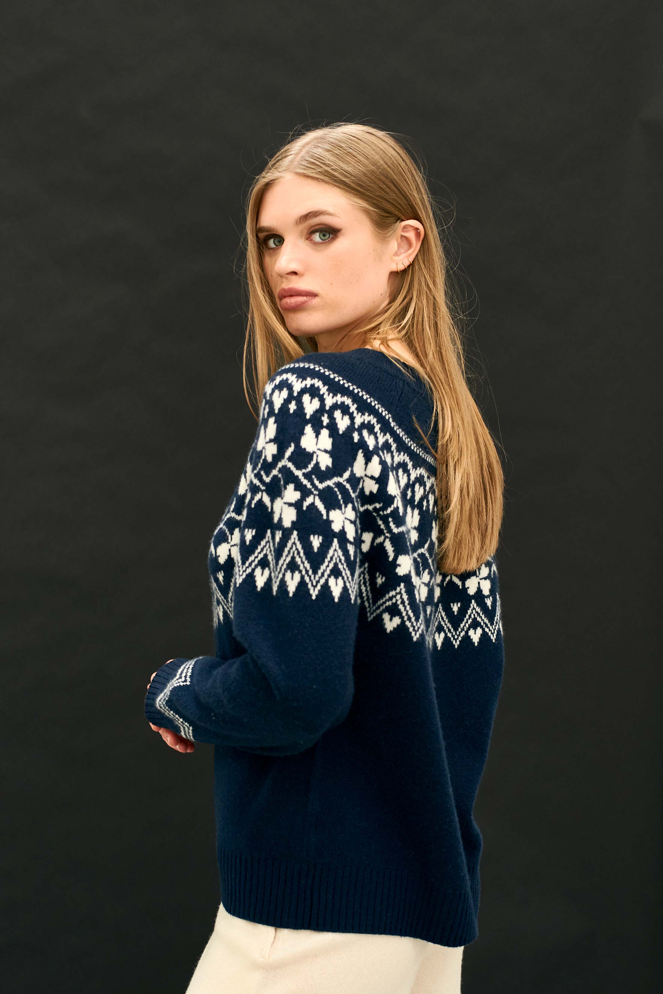 Female model wearing Jumper 1234 navy crew neck jumper in our heavier weight cashmere and wool with a stone clover pattern on the yoke, back and front facing away from the camera
