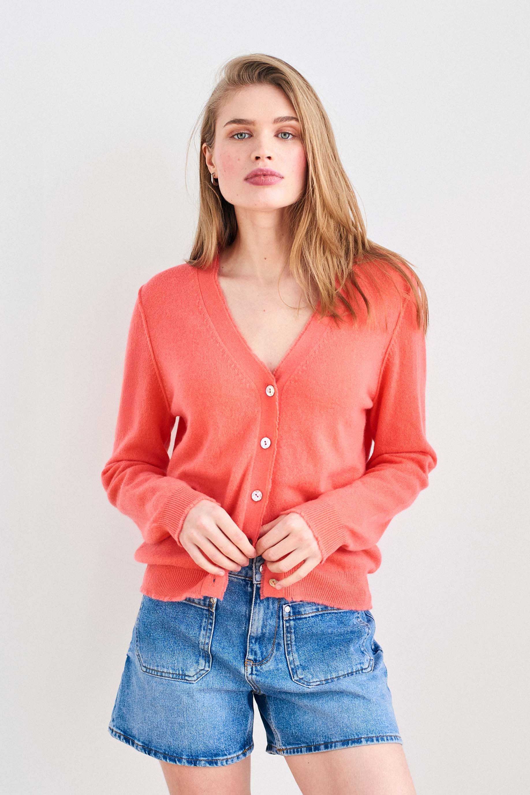 Blonde female model wearing Jumper 1234 Coral cashmere vee neck cardigan with 'distressed' ribs.
