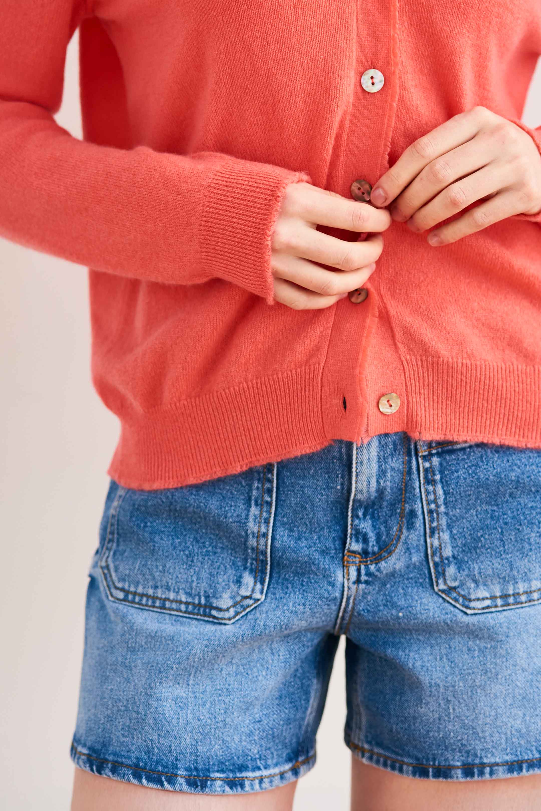 Blonde female model wearing Jumper 1234 Coral cashmere vee neck cardigan with 'distressed' ribs close up