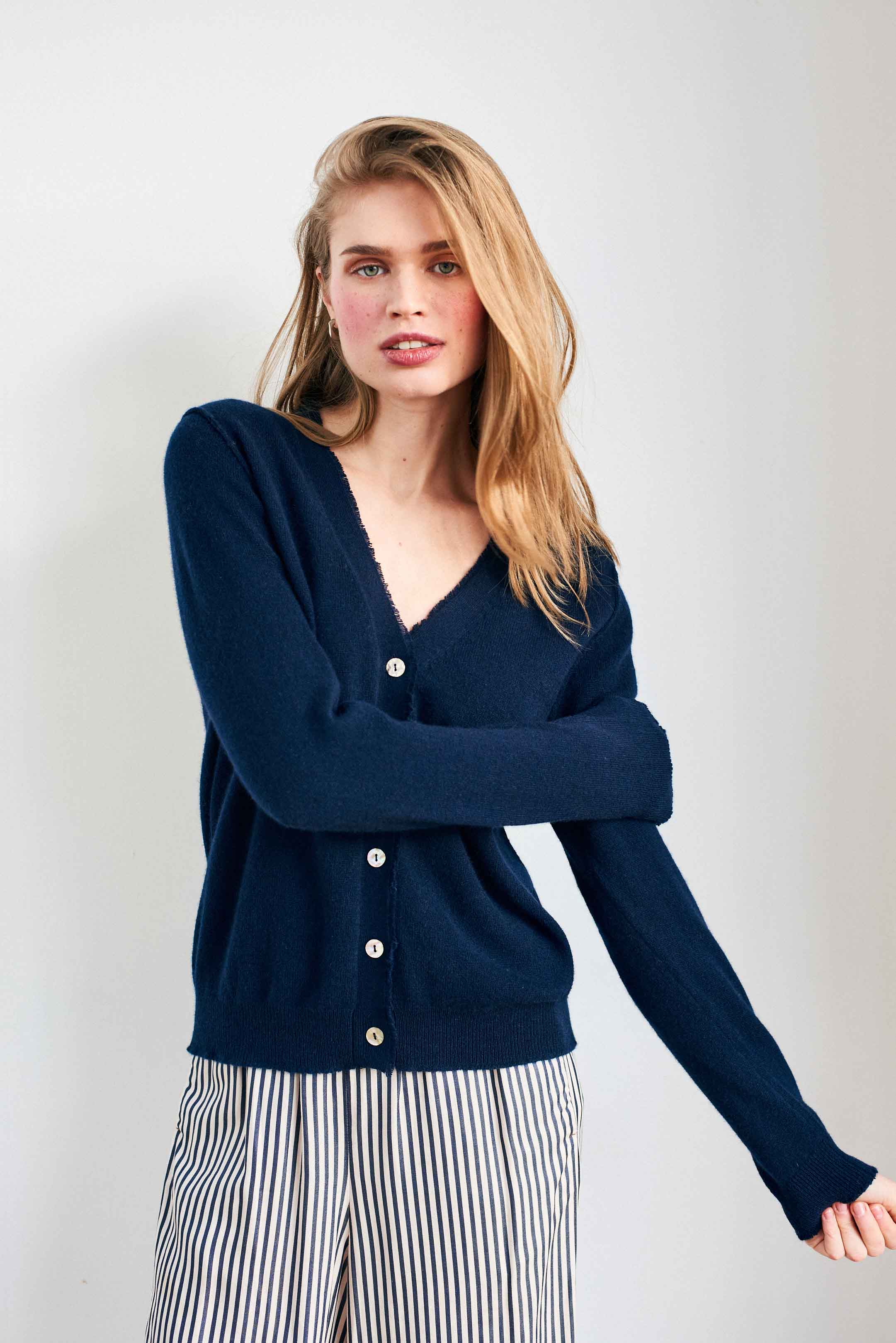 Blonde female model wearing Jumper 1234 Navy cashmere vee neck cardigan with 'distressed' ribs.