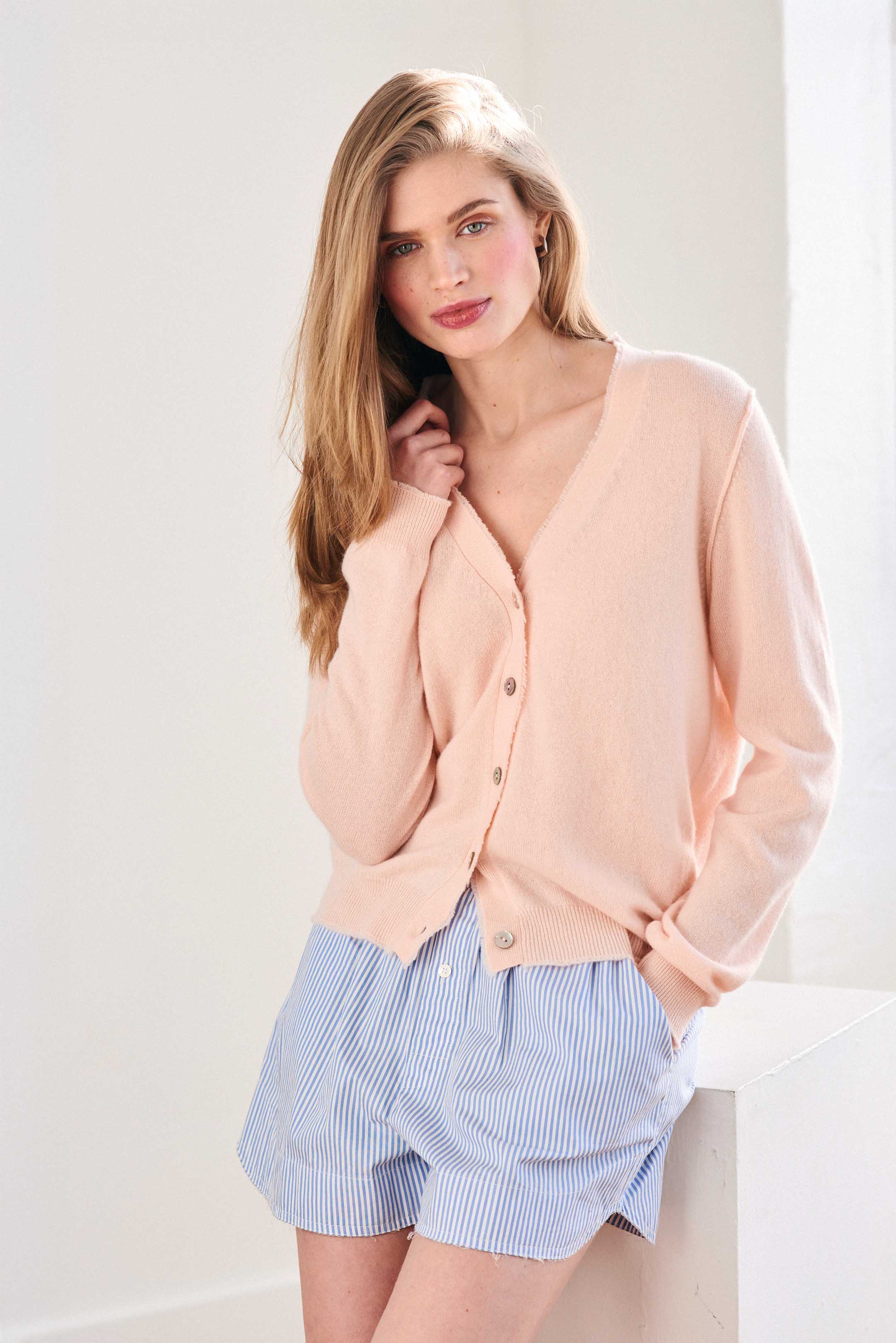 Blonde female model wearing Jumper 1234 pale Pink cashmere vee neck cardigan with 'distressed' ribs.