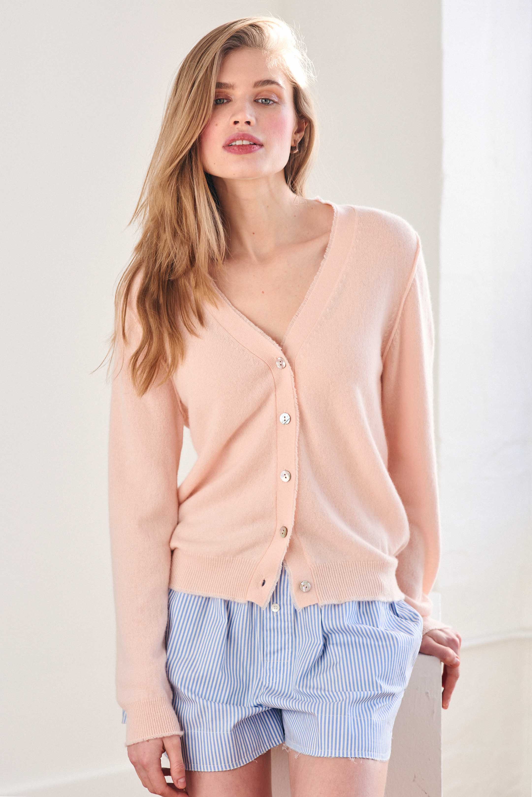 Blonde female model wearing Jumper 1234 Pale Pink cashmere vee neck cardigan with 'distressed' ribs