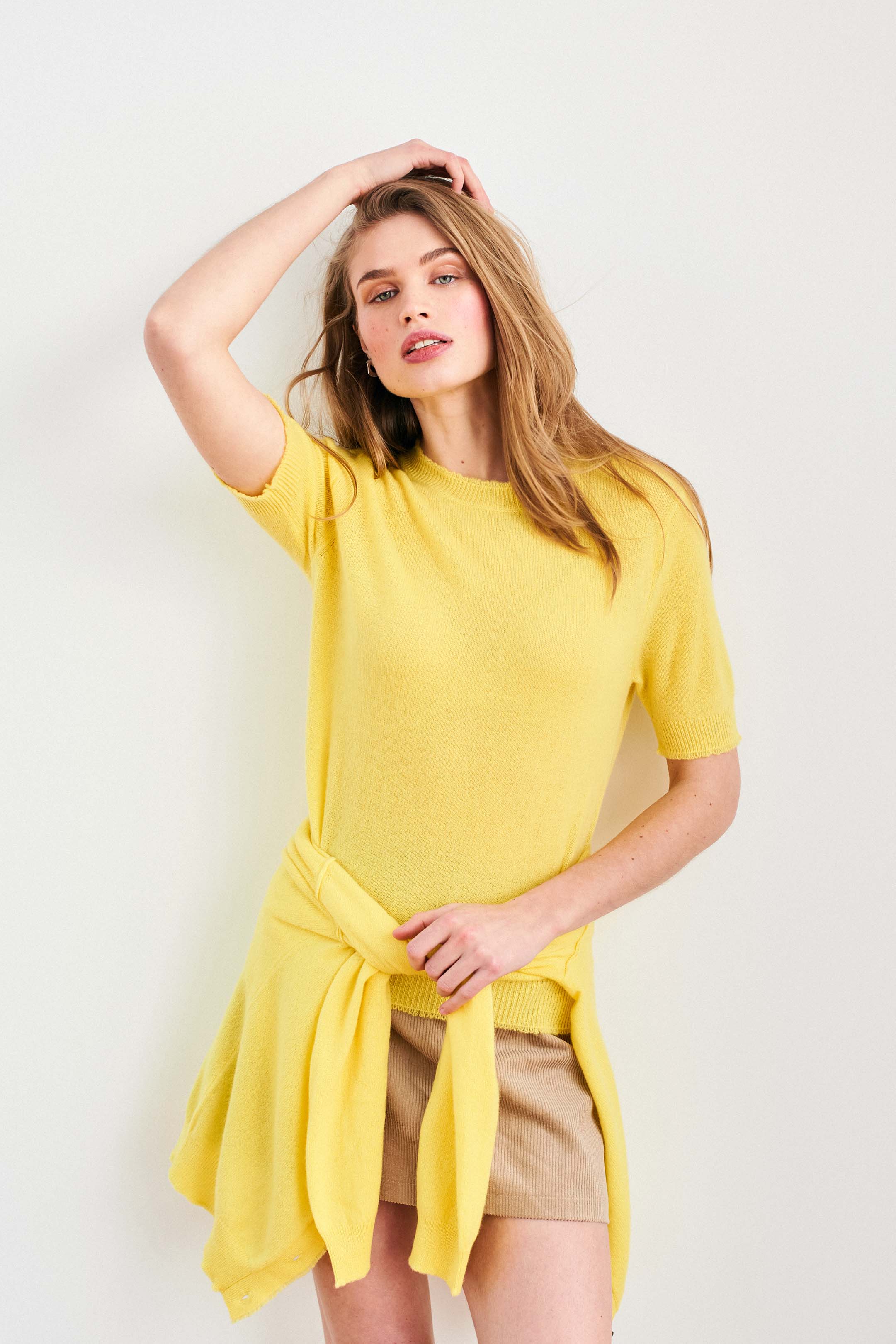 Female model wearing Jumper 1234 Yellow short sleeve cashmere jumper with 'distressed' ribs. With matching cardigan toed around her waist