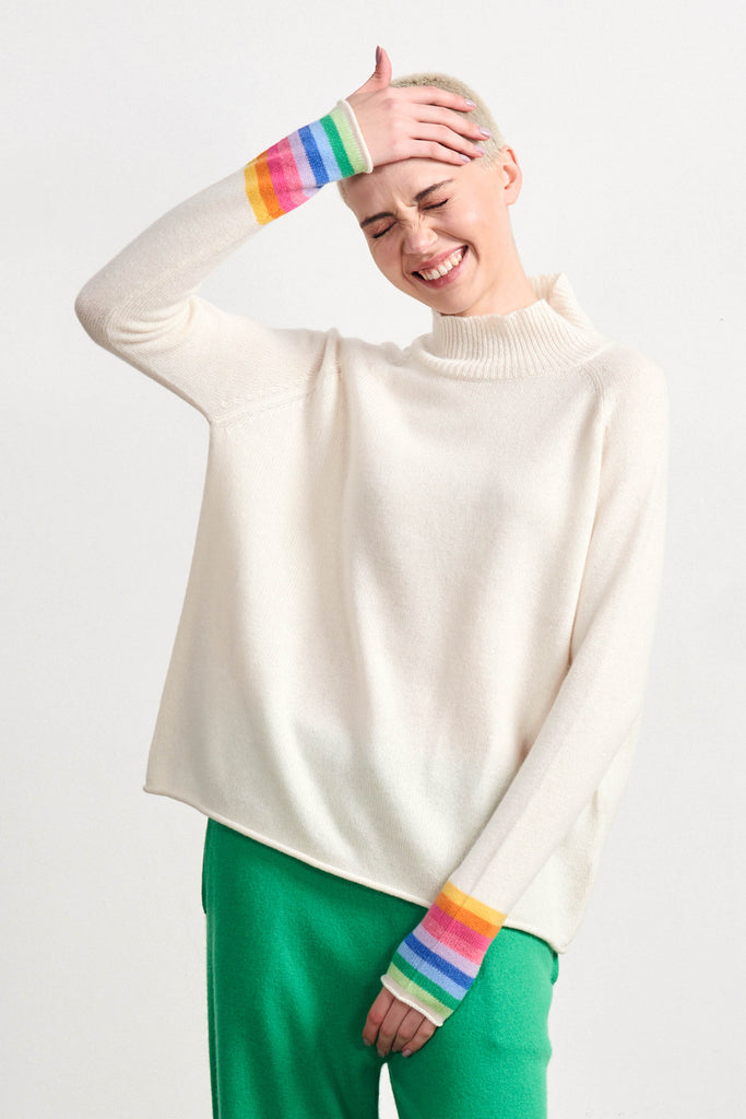 Blonde female model wearing Jumper1234 cream cashmere turtle neck jumper with multicoloured stripes on the cuffs