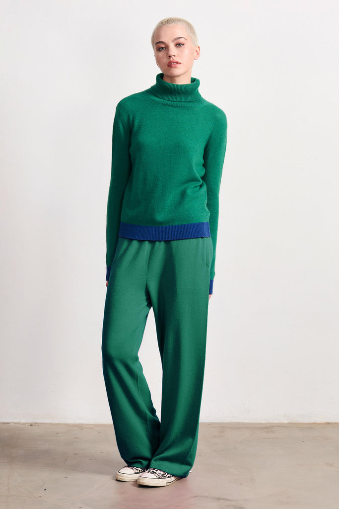 Blonde female model wearing Jumper 1234 grass green cashmere roll neck with contrast denim ribs