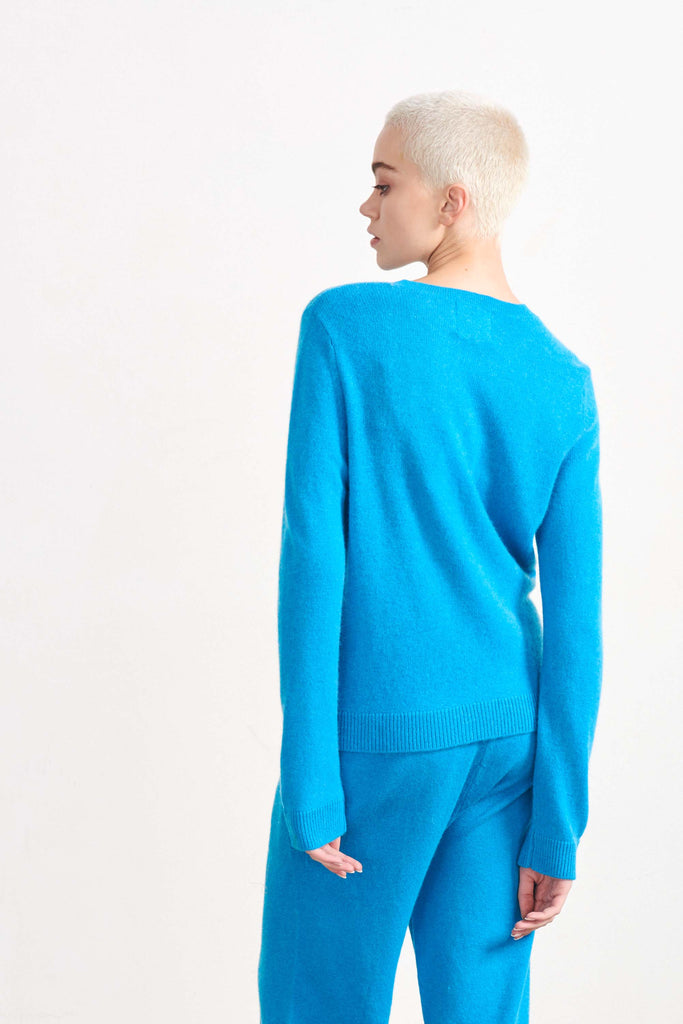 Blonde female model wearing Jumper1234 lightweight cashmere crew in Aqua facing away from the camera