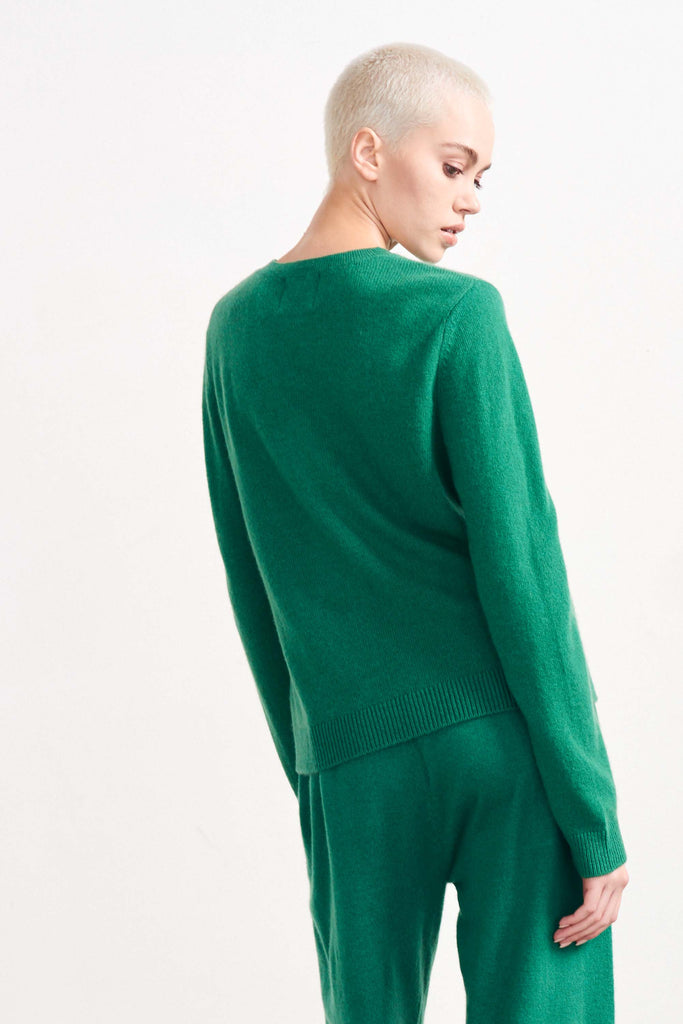Blonde female model wearing Jumper1234 lightweight cashmere crew in Grass Green facing away from the camera