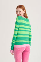 Red haired female model wearing Jumper1234 bright green and neon green stripe crew neck cashmere jumper with rose pink contrast trims facing away from the camera