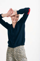 Blonde female model smiling wearing Jumper 1234 cashmere heart patch cardigan in navy with red heart elbow patches