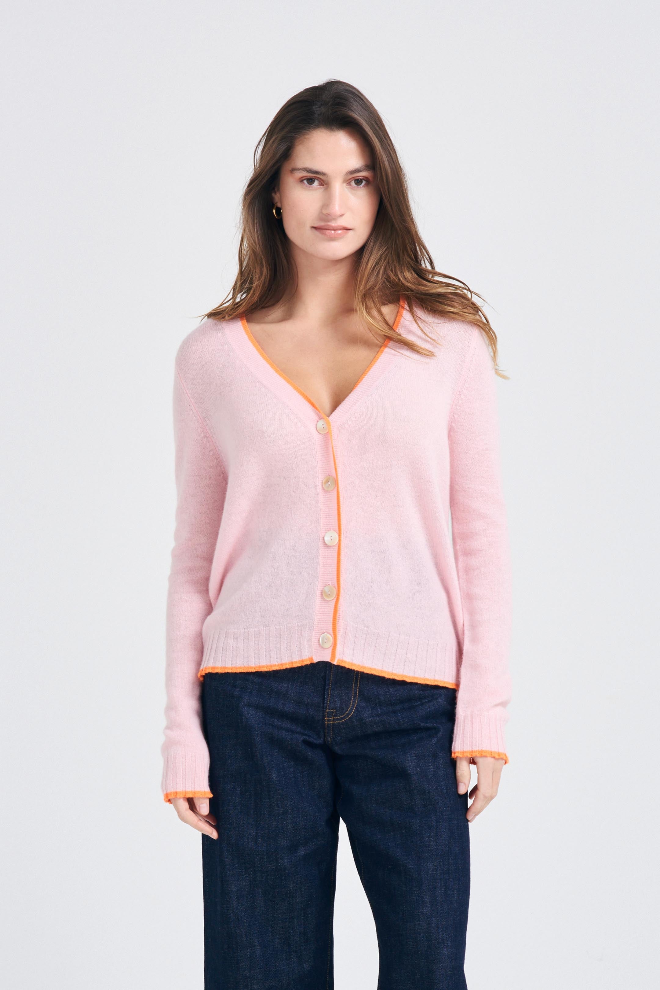 Brown haired female model wearing Jumper1234 Pale pink cashmere vee neck cardigan with neon orange tipping