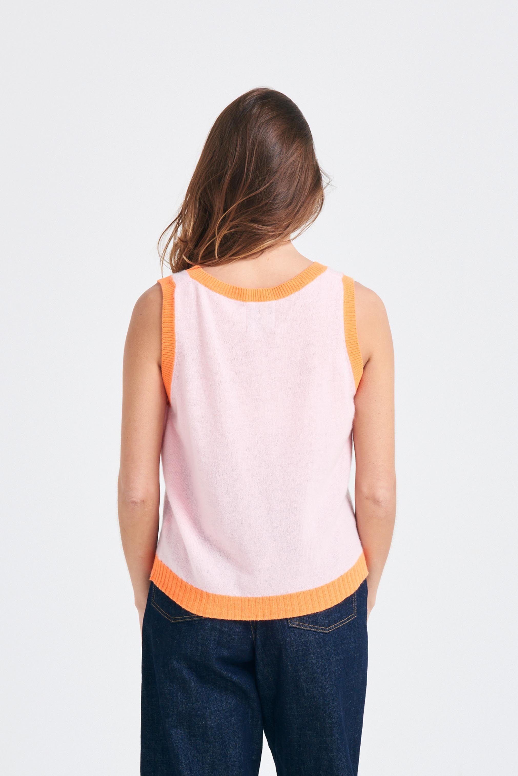 Brown haired female model wearing Jumper1234 Pale pink cashmere vee neck tank with contrast neon orange ribs facing away from the camera