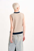 Blonde female model wearing Jumper1234 Organic light brown cashmere vee neck sleeveless cardigan with contrast double ribs in navy and oatmeal facing away from the camera