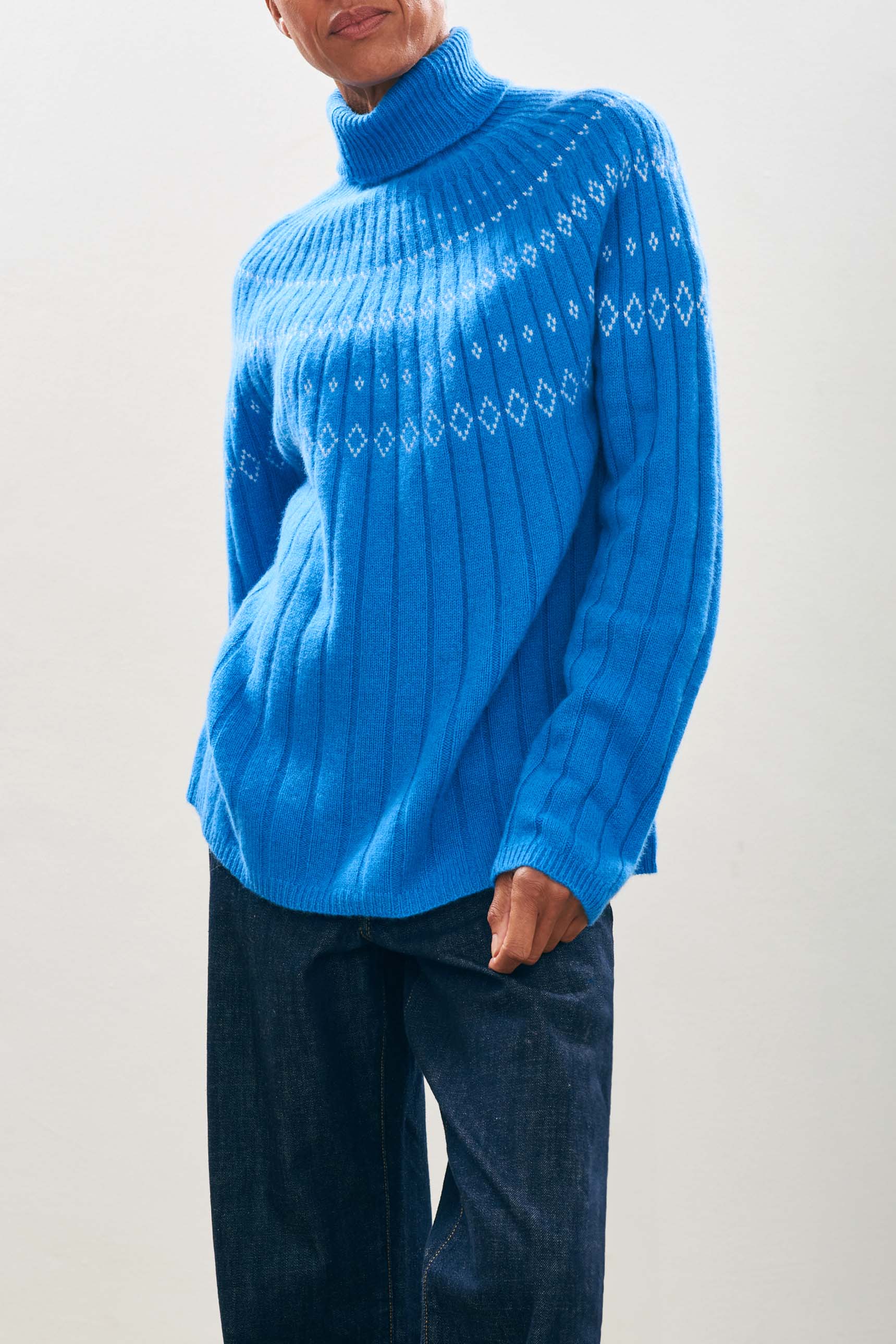 Female model wearing Jumper1234 Cashmere Rib Ski Roll Collar in Sky blue and Cream with fair isle pattern on front and back yolk 