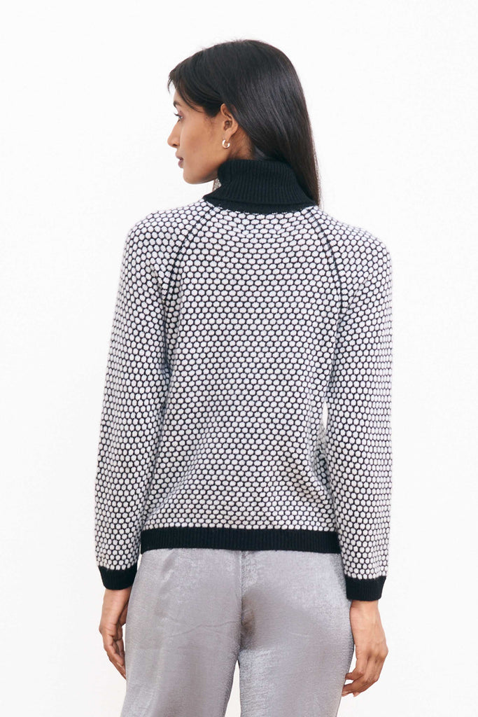 Brown haired female model wearing Jumper1234 "honeycomb" cashmere roll neck in black and pale grey circular contrast knit facing away from the camera