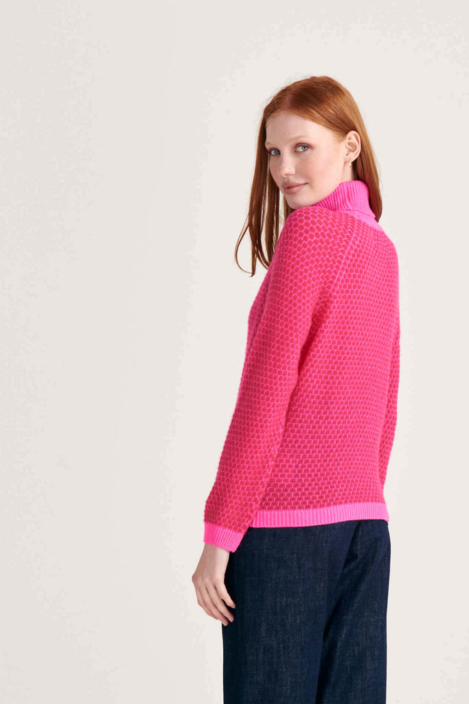Ginger female model wearing Jumper1234 "honeycomb" cashmere roll neck in hot pink and cherry circular contrast knit facing away from the camera