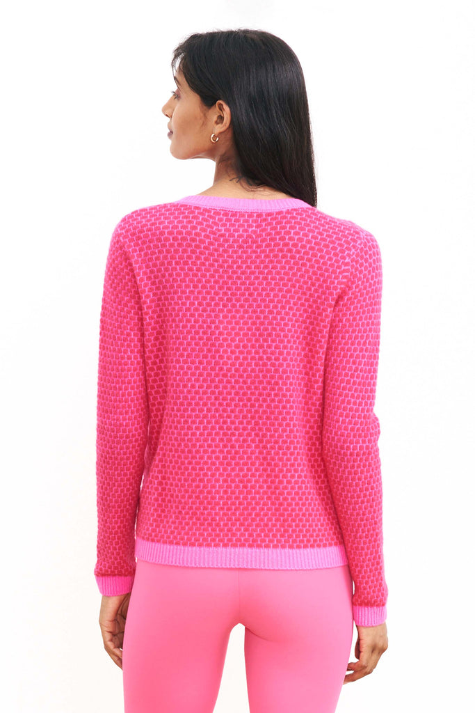 Brown haired female model wearing Jumper1234 "honeycomb" cashmere vee neck in hot pink and cherry circular contrast knit facing away from the camera