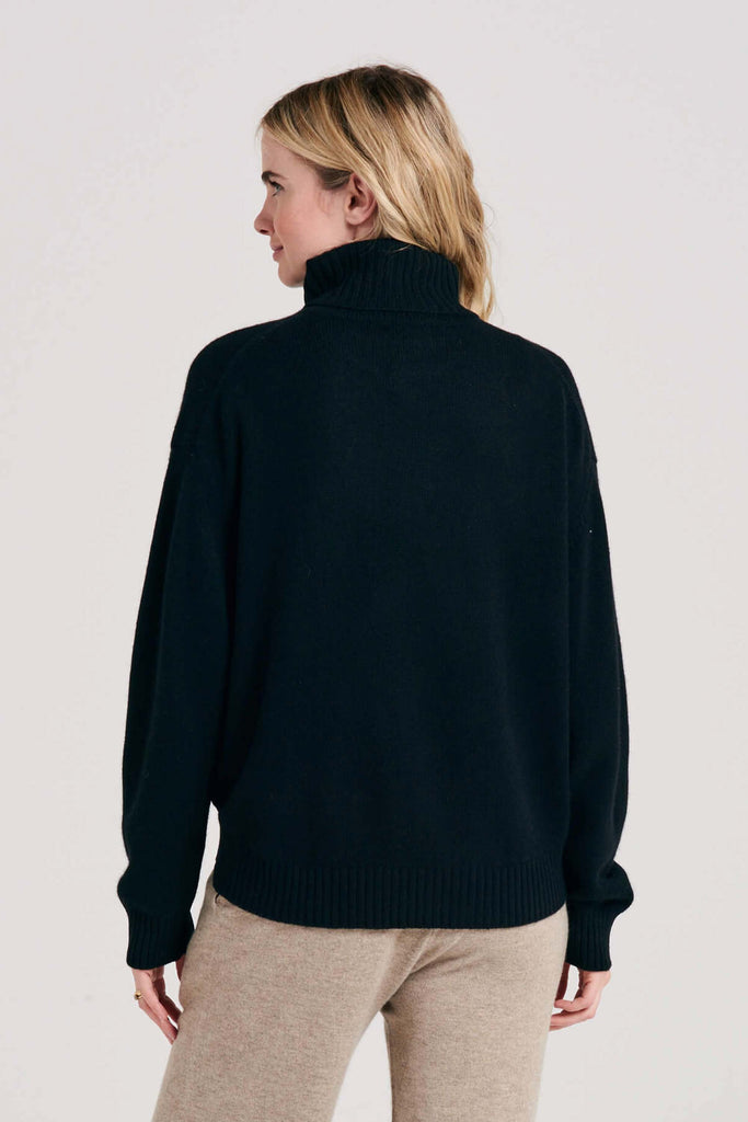 Blonde female model wearing Jumper1234 oversized cashmere roll collar in black facing away from the camera