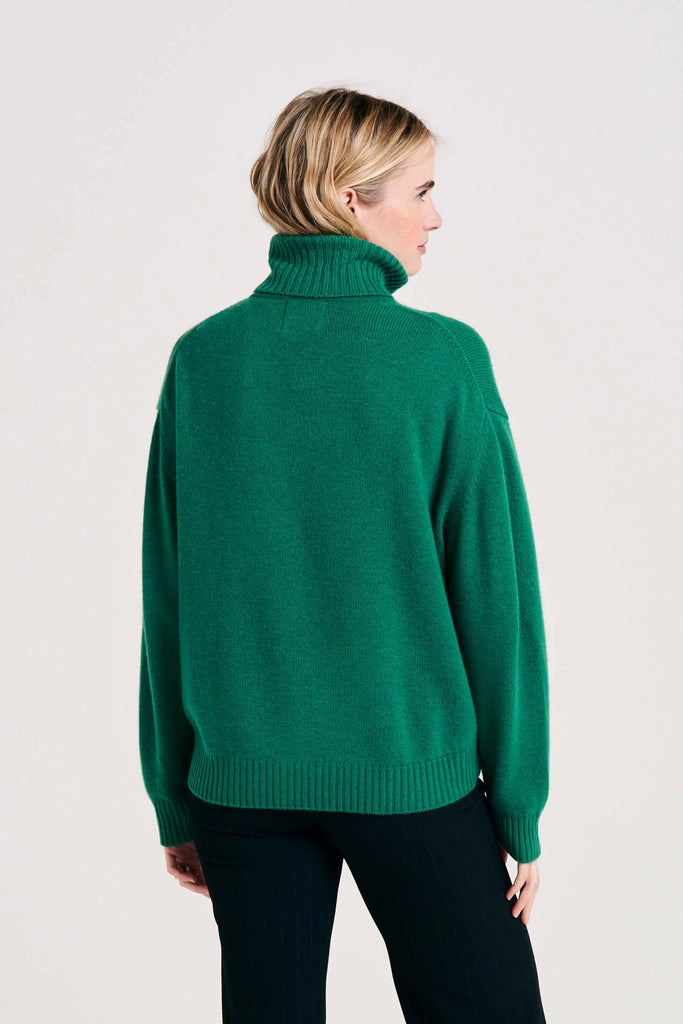 Blonde female model wearing Jumper1234 oversized cashmere roll collar in grass green facing away from the camera
