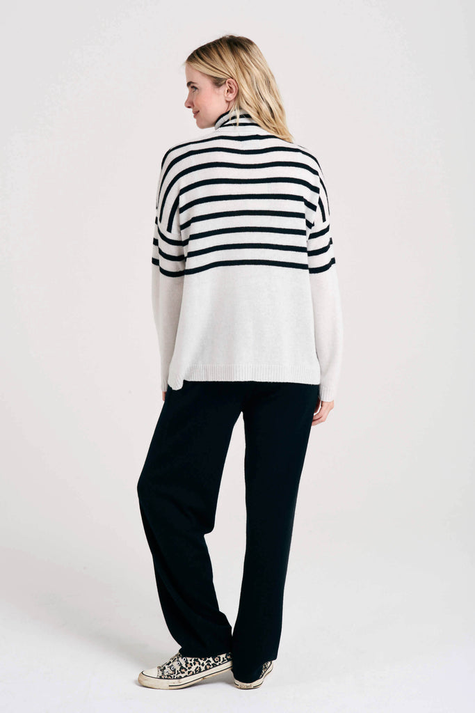 Blonde female model wearing Jumper1234 white cashmere roll neck with half black stripe detail facing away from the camera