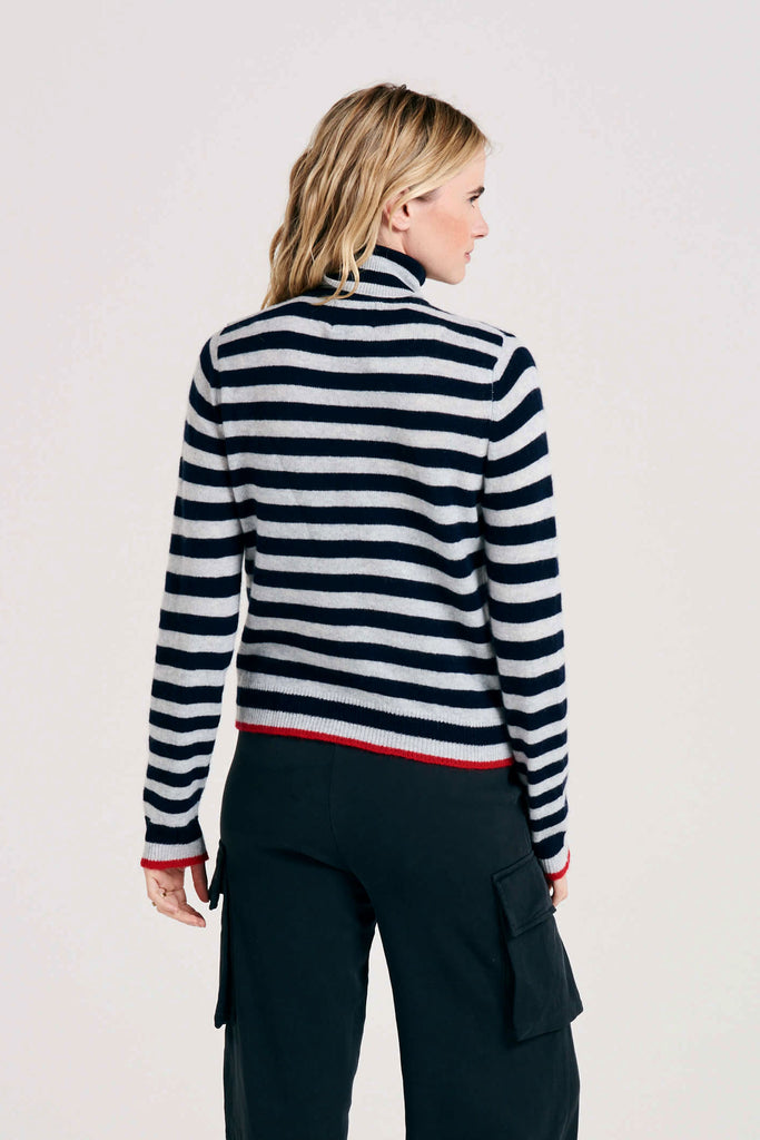 Blonde female model wearing Jumper 1234 grass navy and silver stripe cashmere roll neck with contrast red ribs facing away from the camera