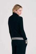 Blonde female model wearing Jumper1234 black cashmere roll collar with contrasting mid grey ribs facing away from the camera