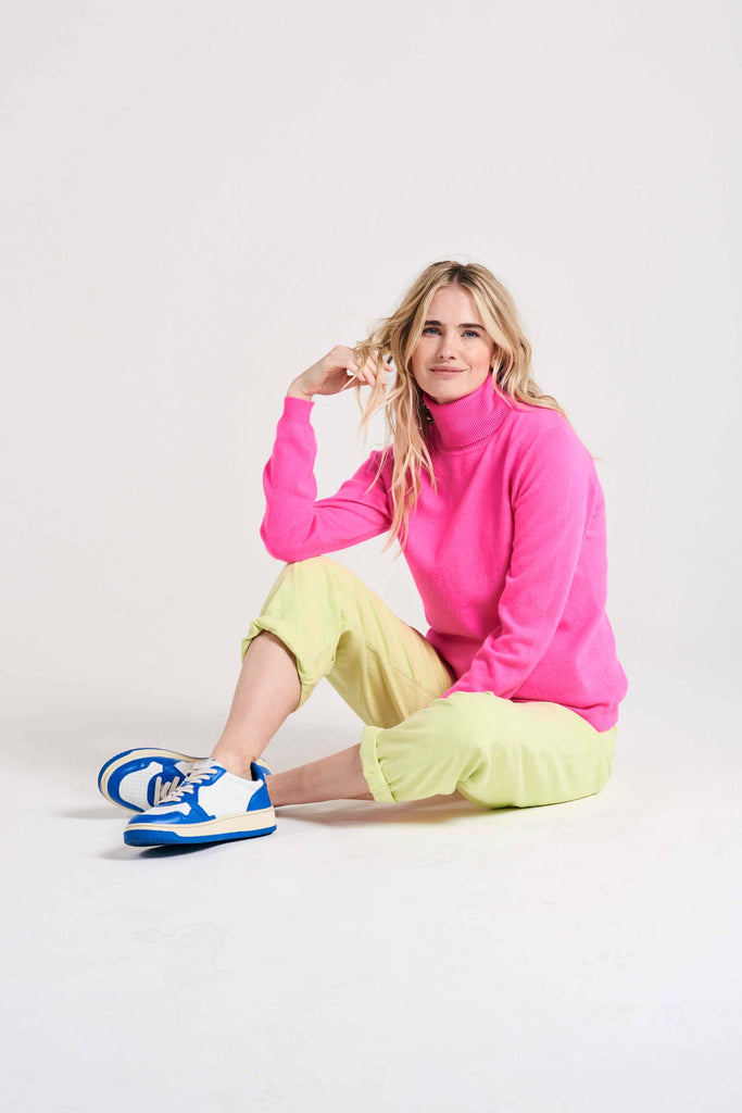 Blonde female model sat wearing Jumper1234 hot pink cashmere roll neck
