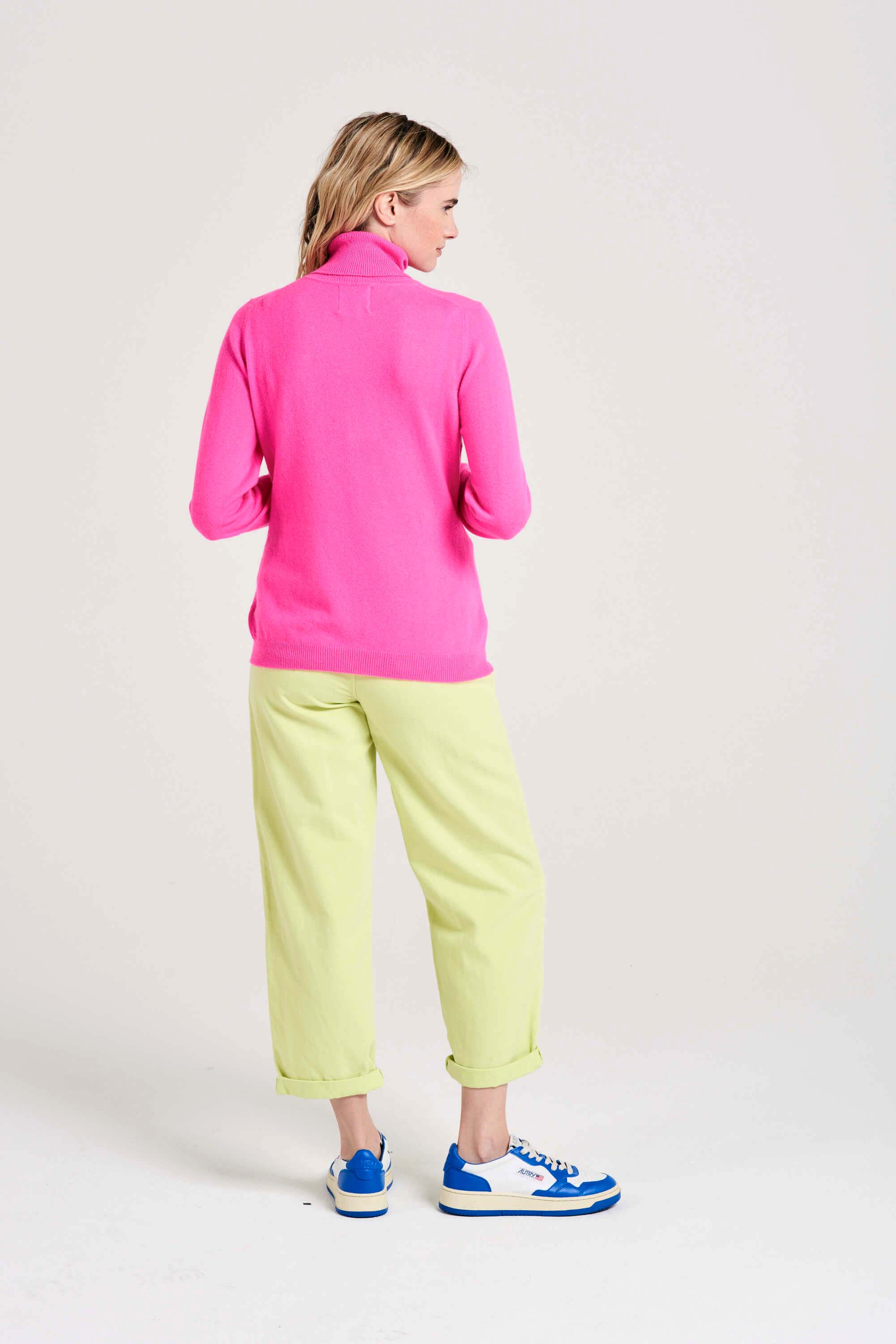 Blonde female model wearing Jumper1234 hot pink cashmere roll neck facing away from the camera