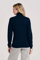 Blonde female model wearing Jumper1234 navy cashmere roll neck facing away from the camera