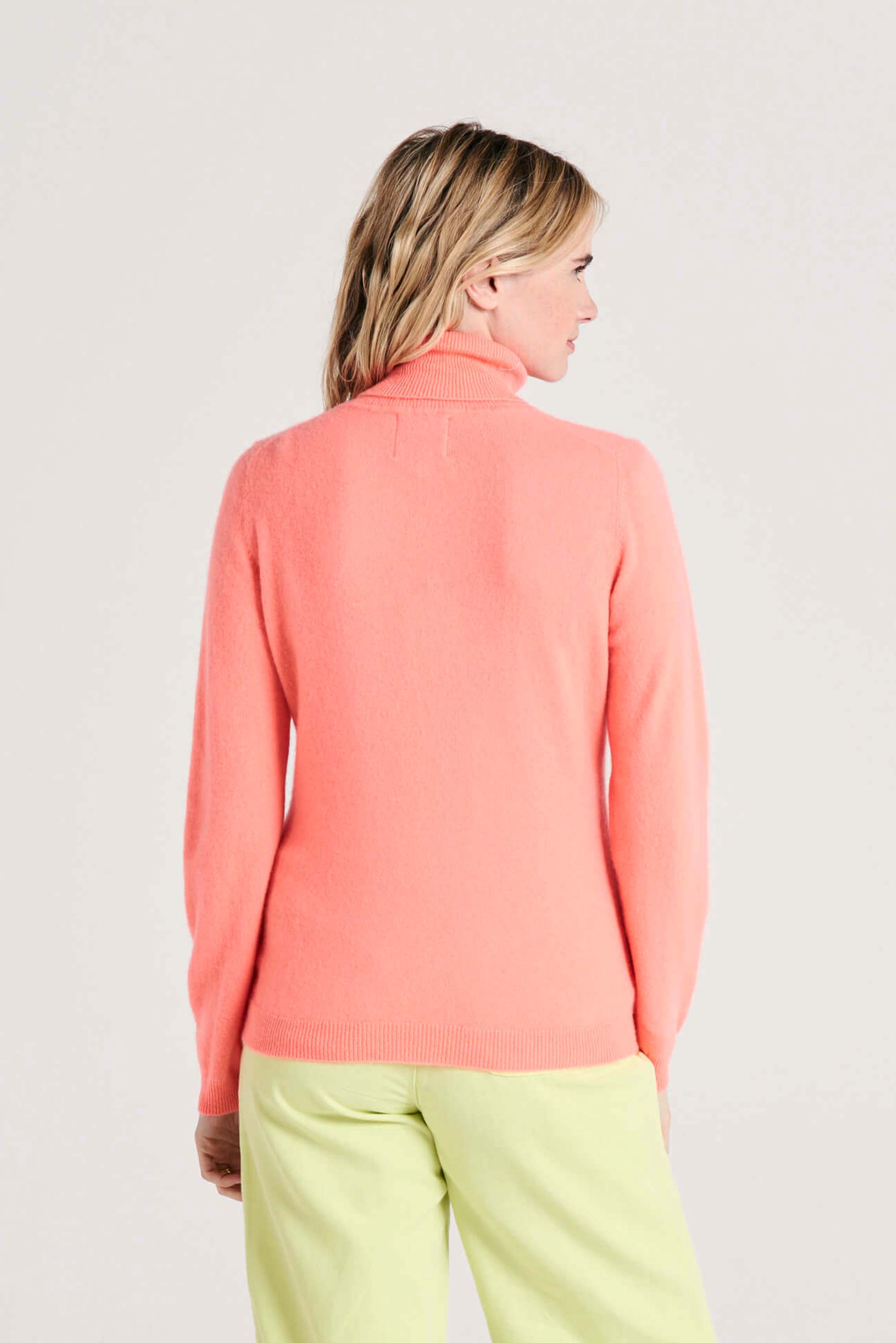 Blonde female model wearing Jumper1234 neon coral cashmere roll neck facing away from the camera