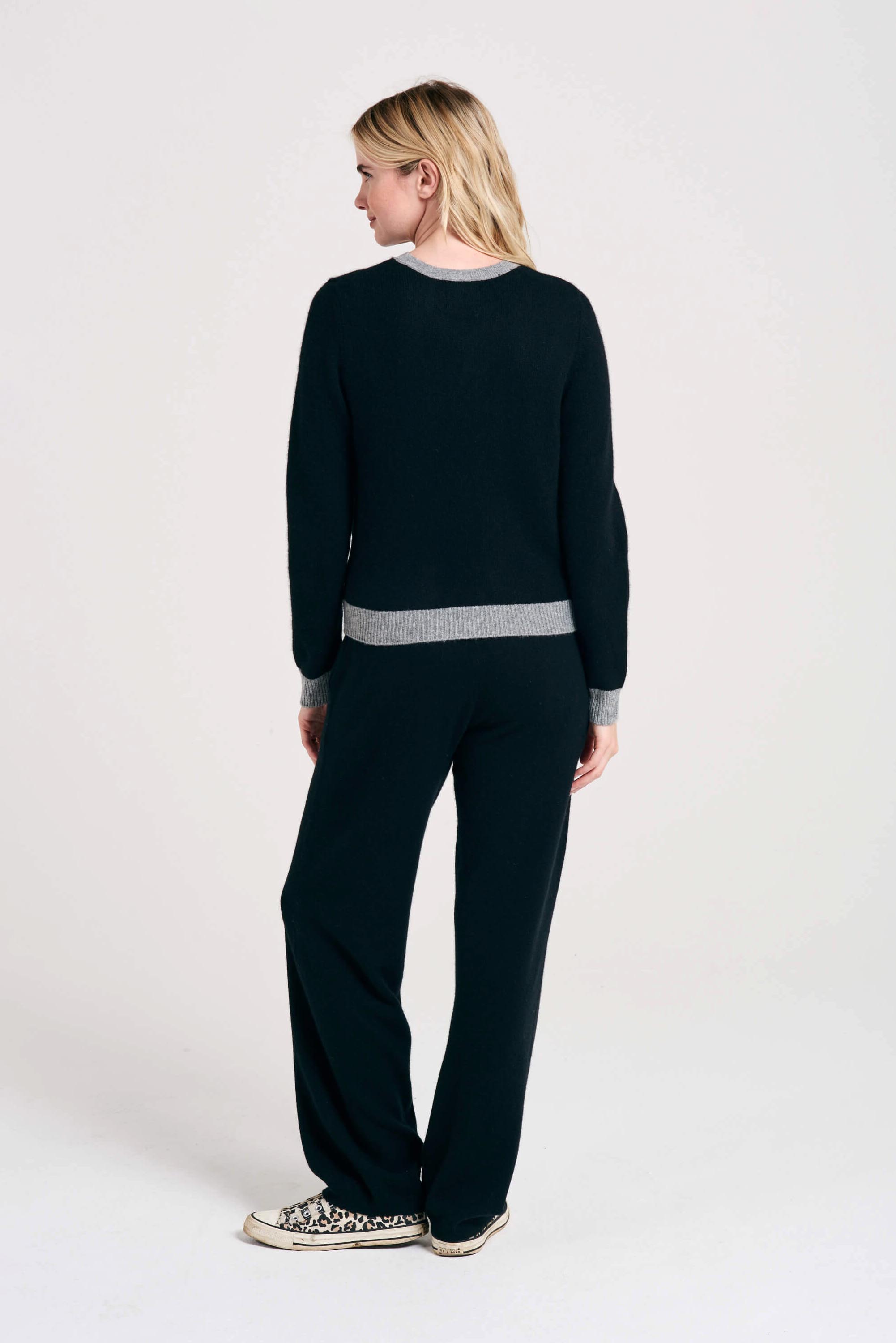 Blonde female model wearing Jumper1234 black cashmere crew neck with mid grey ribs facing away from the camera
