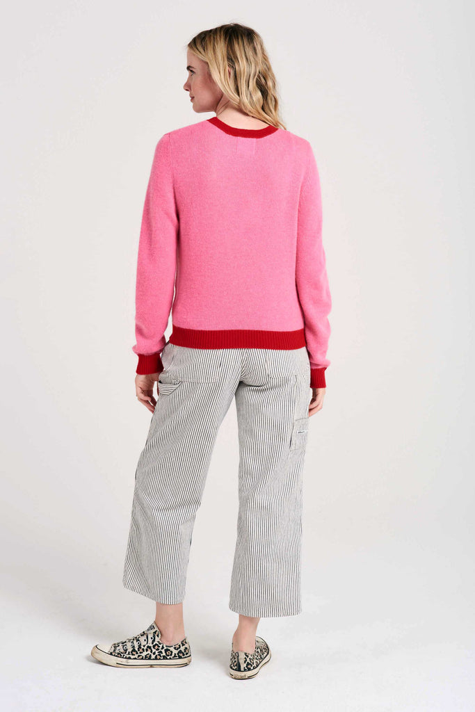 Blonde female model wearing Jumper1234 candy pink cashmere crew neck with red ribs facing away from the camera