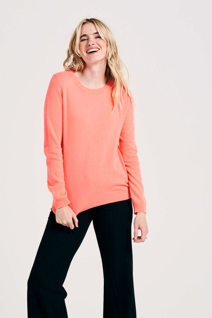 Blonde female model wearing Jumper1234 neon coral cashmere crew with split detail at the wrists and welt