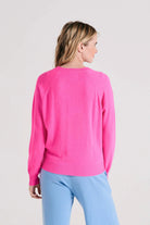 Blonde female model wearing Jumper1234 cashmere raglan vee neck jumper in hot pink facing away from the camera