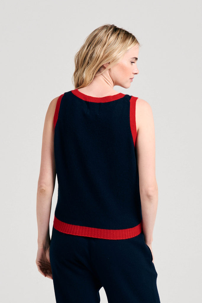 Blonde female model wearing Jumper1234 navy cashmere contrast tank with red ribs facing away from the camera