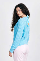 Brown haired female model wearing Jumper1234 Opal cotton aran crew neck jumper with a ribbon tie back facing away from the camera